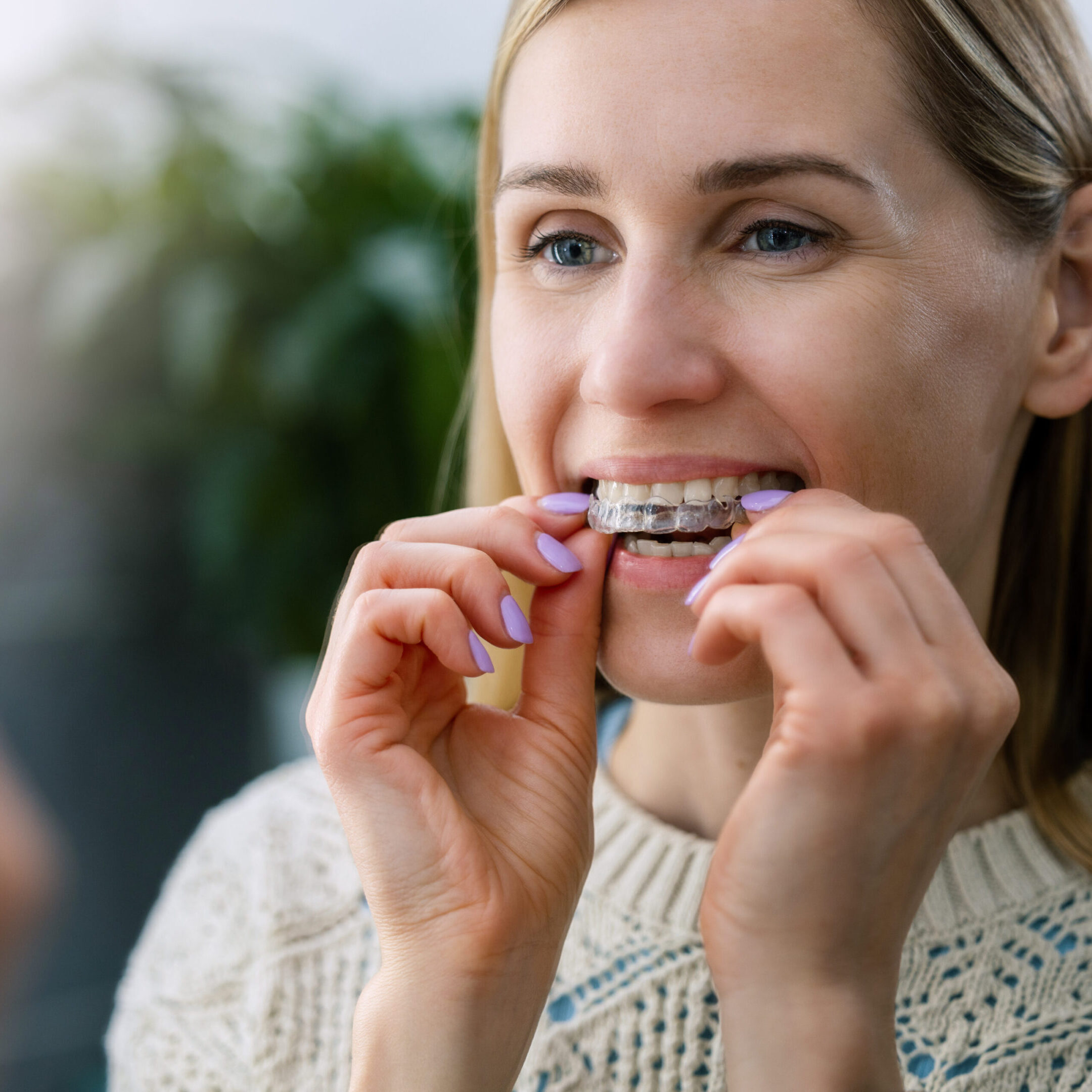 Woman inserting clear dental aligner in mirror
